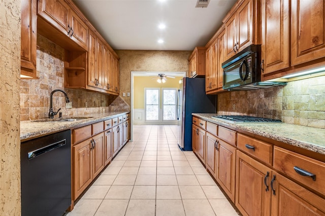 kitchen with brown cabinets, black appliances, a sink, light tile patterned floors, and light stone countertops