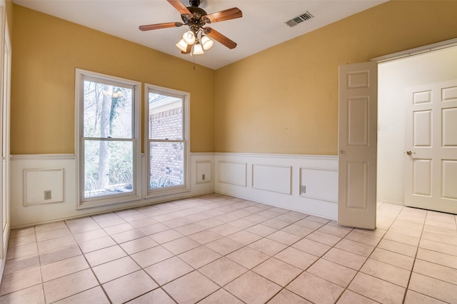 unfurnished room with light tile patterned floors, visible vents, ceiling fan, wainscoting, and a decorative wall