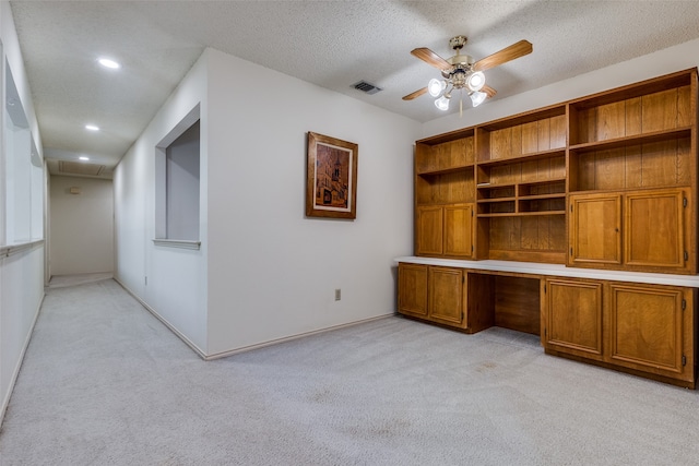 unfurnished office featuring light carpet, a textured ceiling, built in desk, and ceiling fan