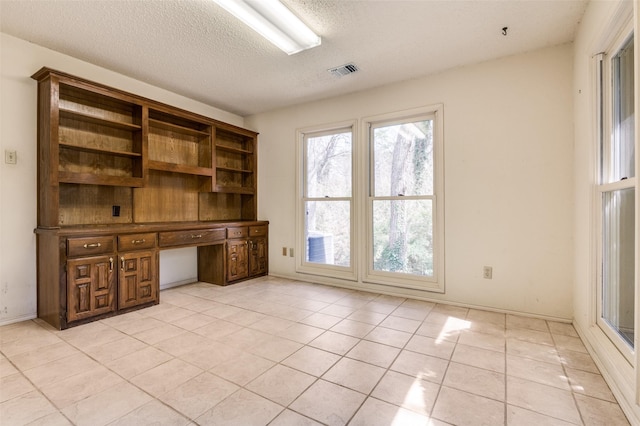 unfurnished office featuring light tile patterned floors, visible vents, a textured ceiling, and built in study area