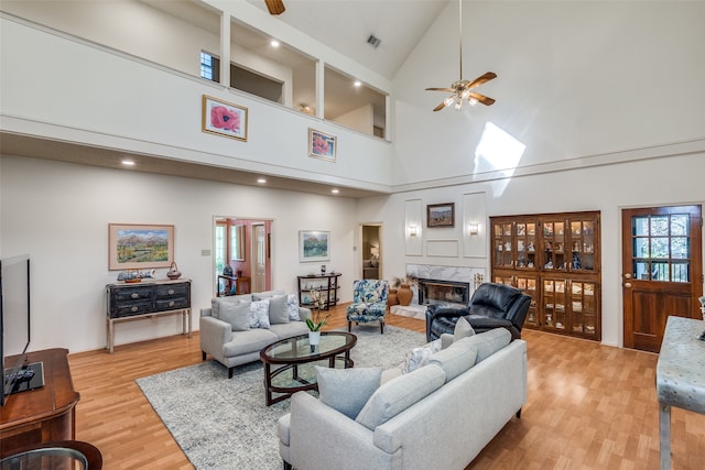 living room featuring high vaulted ceiling, light hardwood / wood-style floors, ceiling fan, and a fireplace