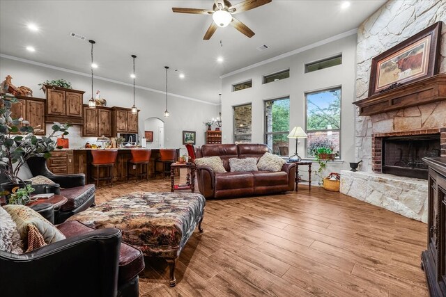 living room with a stone fireplace, light wood-type flooring, ceiling fan with notable chandelier, and ornamental molding