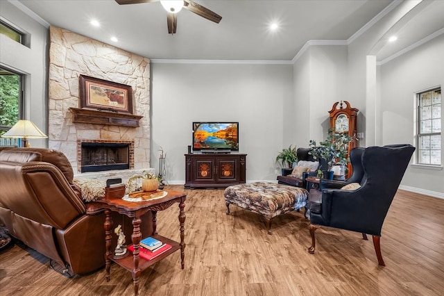 living room featuring ceiling fan, hardwood / wood-style flooring, crown molding, and a fireplace