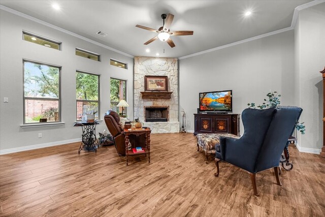 living area with a stone fireplace, ceiling fan, crown molding, and light hardwood / wood-style flooring