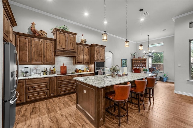 kitchen with a center island with sink, crown molding, stainless steel appliances, pendant lighting, and light hardwood / wood-style floors