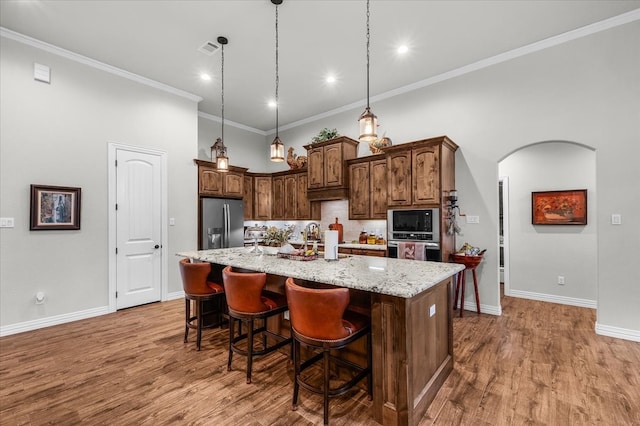 kitchen featuring hardwood / wood-style floors, a kitchen island with sink, crown molding, light stone countertops, and appliances with stainless steel finishes