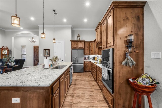 kitchen with stainless steel appliances, light wood-type flooring, decorative light fixtures, sink, and a spacious island