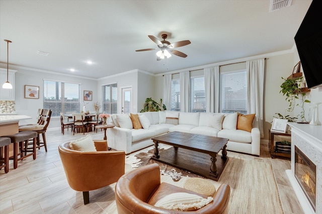 living room with ceiling fan, ornamental molding, a fireplace, and light hardwood / wood-style floors