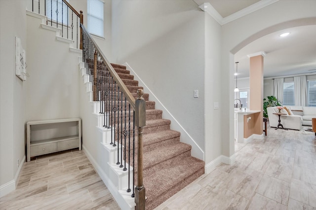 stairway featuring ornamental molding, a towering ceiling, and a wealth of natural light