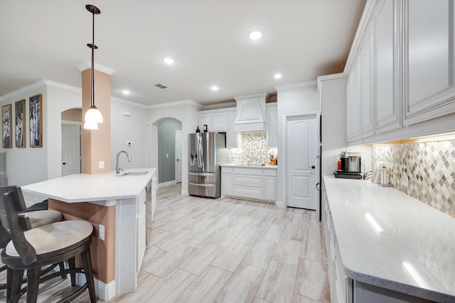 kitchen featuring pendant lighting, white cabinetry, an island with sink, sink, and stainless steel refrigerator with ice dispenser