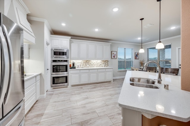 kitchen featuring stainless steel appliances, sink, ornamental molding, hanging light fixtures, and white cabinets