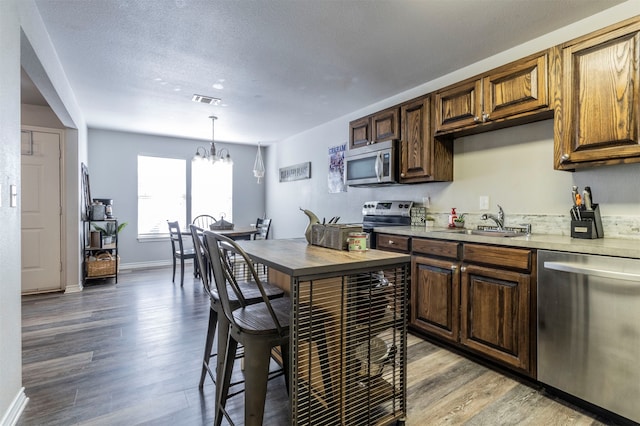 kitchen featuring pendant lighting, sink, stainless steel appliances, a chandelier, and light wood-type flooring