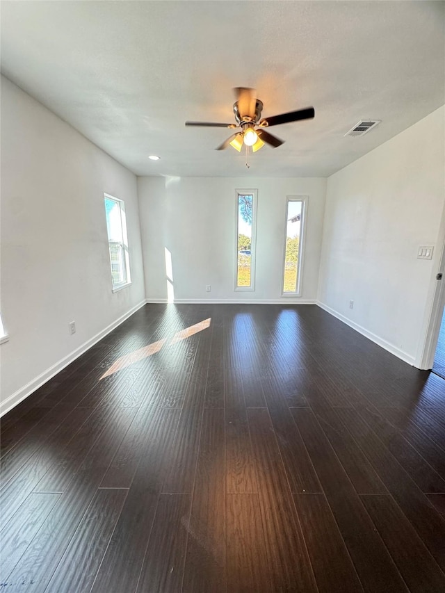 empty room with a healthy amount of sunlight, ceiling fan, and dark wood-type flooring