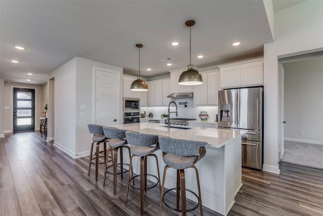 kitchen featuring an island with sink, appliances with stainless steel finishes, white cabinets, and decorative light fixtures