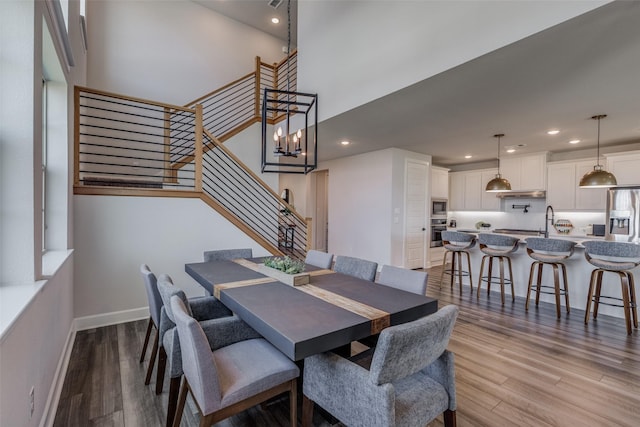 dining area featuring a towering ceiling, sink, and light wood-type flooring