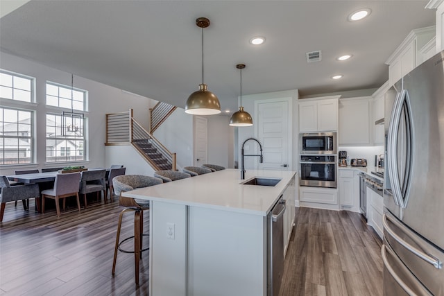 kitchen with sink, white cabinetry, decorative light fixtures, appliances with stainless steel finishes, and an island with sink