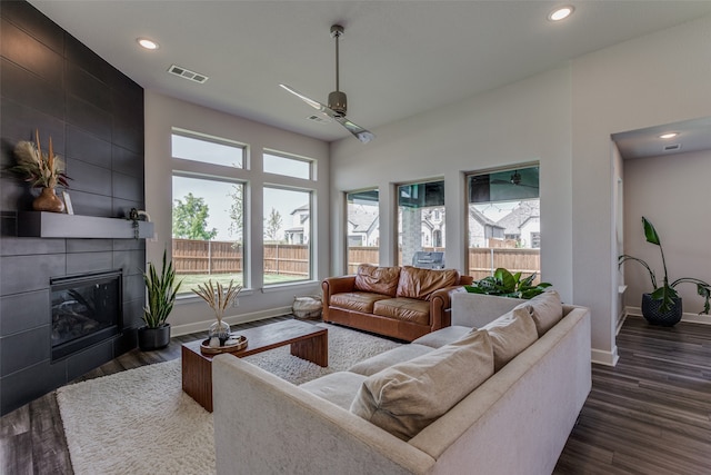 living room featuring dark wood-type flooring, ceiling fan, and a tiled fireplace