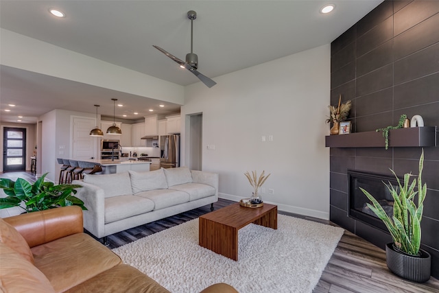 living room featuring light hardwood / wood-style flooring, a tile fireplace, and ceiling fan