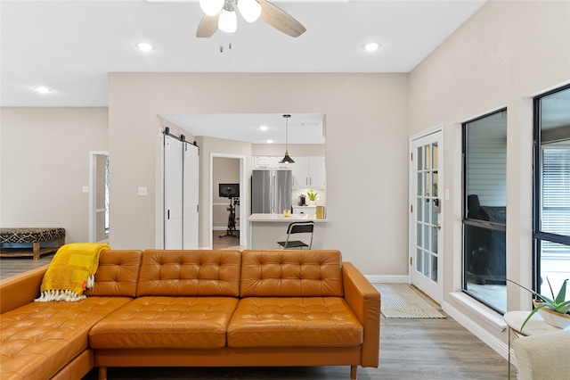 living room with hardwood / wood-style flooring, a barn door, and ceiling fan