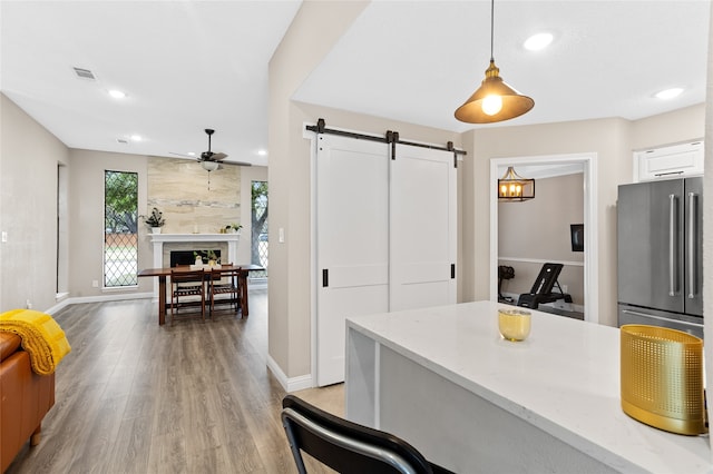 kitchen with stainless steel fridge, white cabinetry, a barn door, hanging light fixtures, and light hardwood / wood-style flooring