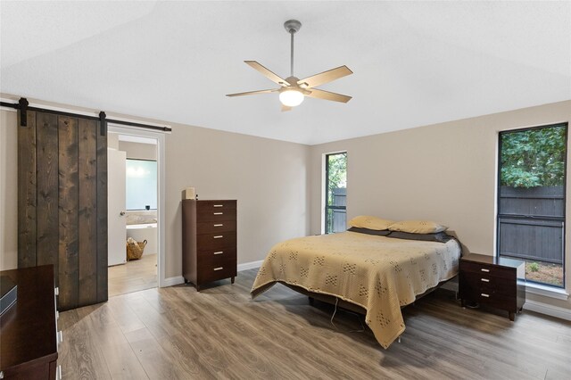 bedroom with ensuite bath, wood-type flooring, lofted ceiling, a barn door, and ceiling fan