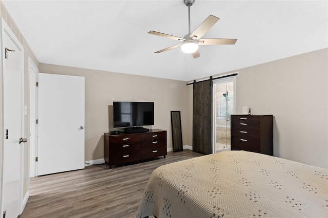 bedroom featuring hardwood / wood-style floors, a barn door, ceiling fan, and connected bathroom