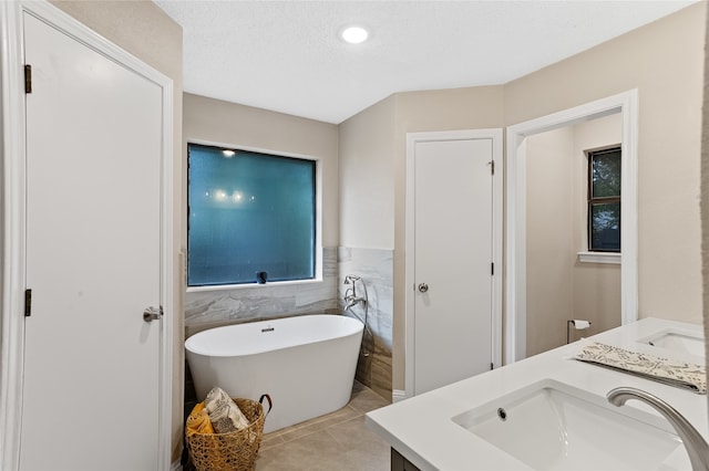 bathroom with tile patterned flooring, a textured ceiling, vanity, a bathing tub, and tile walls