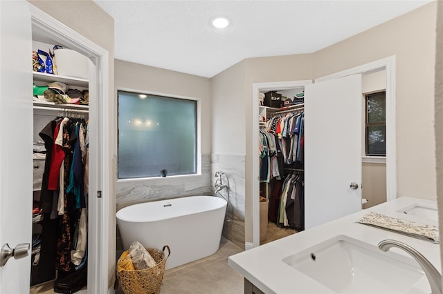 bathroom featuring a tub, tile walls, tile patterned flooring, a textured ceiling, and vanity