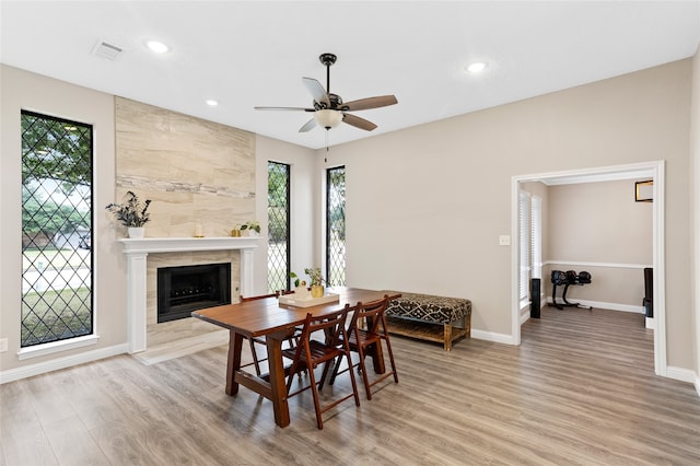 dining space featuring a tile fireplace, ceiling fan, and light hardwood / wood-style flooring