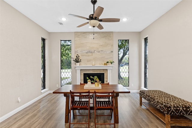 dining room featuring wood-type flooring, a tile fireplace, and ceiling fan