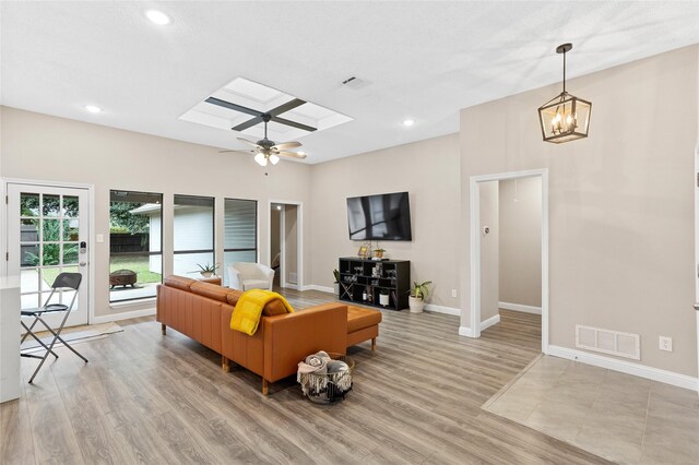 living room featuring a skylight, light hardwood / wood-style floors, and ceiling fan with notable chandelier