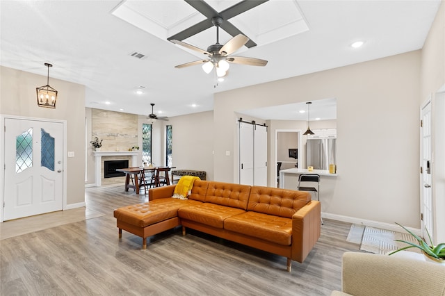 living room with a barn door, a premium fireplace, ceiling fan, and light wood-type flooring