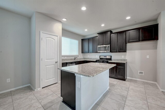 kitchen featuring light stone counters, appliances with stainless steel finishes, light tile patterned floors, sink, and a center island