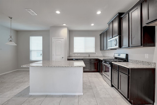 kitchen with light stone counters, appliances with stainless steel finishes, decorative light fixtures, sink, and a center island