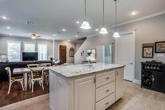 kitchen featuring a kitchen island, pendant lighting, white cabinetry, crown molding, and light stone countertops