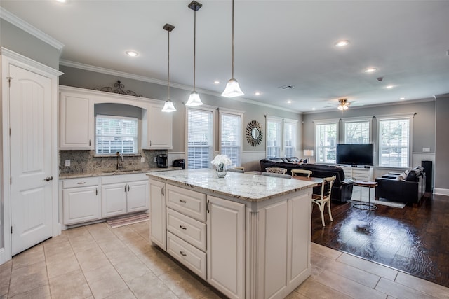 kitchen featuring light stone counters, a kitchen island, white cabinetry, appliances with stainless steel finishes, and decorative light fixtures