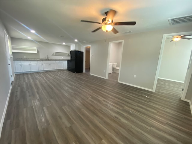 kitchen with black fridge, dark hardwood / wood-style flooring, light stone countertops, sink, and white cabinets