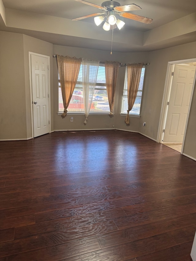 empty room with dark hardwood / wood-style floors, ceiling fan, and a tray ceiling