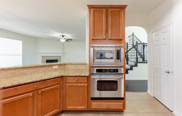 kitchen featuring light stone countertops, appliances with stainless steel finishes, light tile patterned floors, and ceiling fan