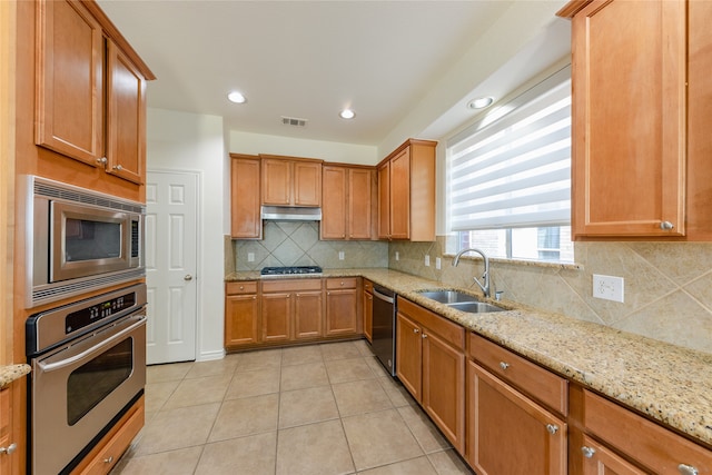 kitchen with appliances with stainless steel finishes, sink, light stone counters, and light tile patterned floors