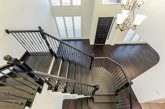 stairs featuring a towering ceiling, hardwood / wood-style flooring, and a chandelier