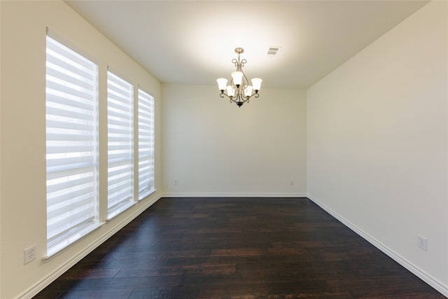 empty room featuring an inviting chandelier and dark hardwood / wood-style floors