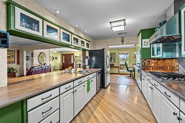 kitchen with white cabinetry, light wood-type flooring, sink, and wall chimney range hood