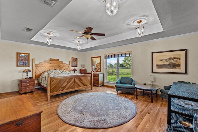 bedroom with ornamental molding, light hardwood / wood-style flooring, and a raised ceiling