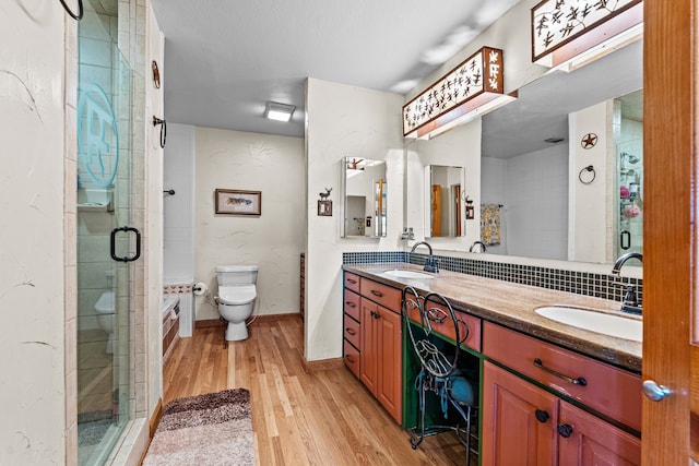 bathroom with toilet, a shower with door, hardwood / wood-style floors, vanity, and backsplash