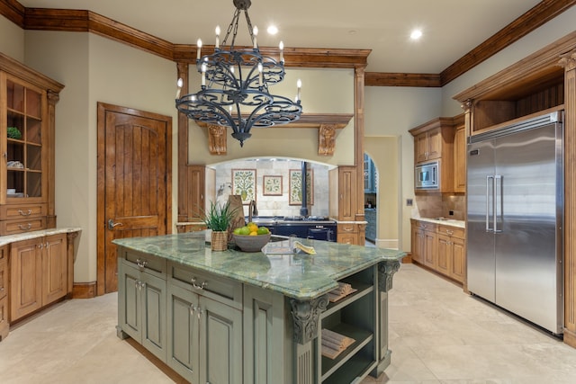 kitchen with light stone counters, built in appliances, decorative light fixtures, a notable chandelier, and a kitchen island