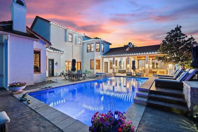 pool at dusk with outdoor lounge area, a patio area, and an in ground hot tub