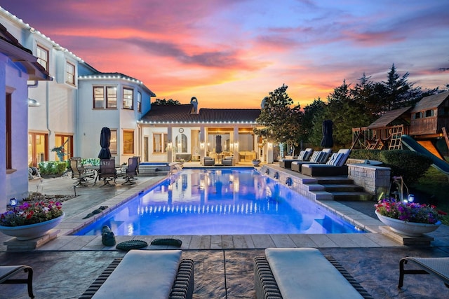 pool at dusk featuring a playground and a patio area