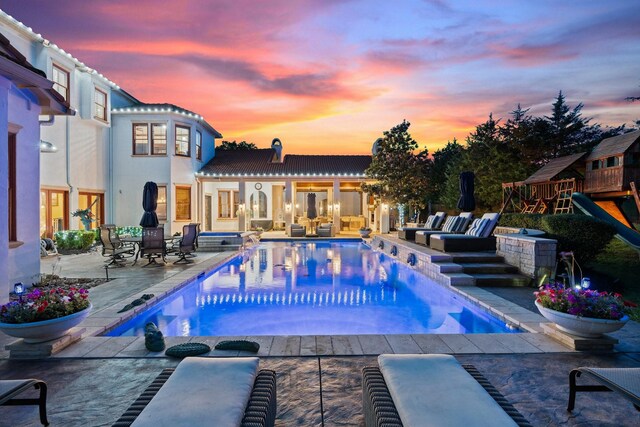 pool at dusk with a jacuzzi, a patio, and a playground