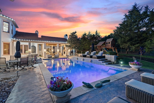 pool at dusk featuring an outdoor structure, a playground, and a patio